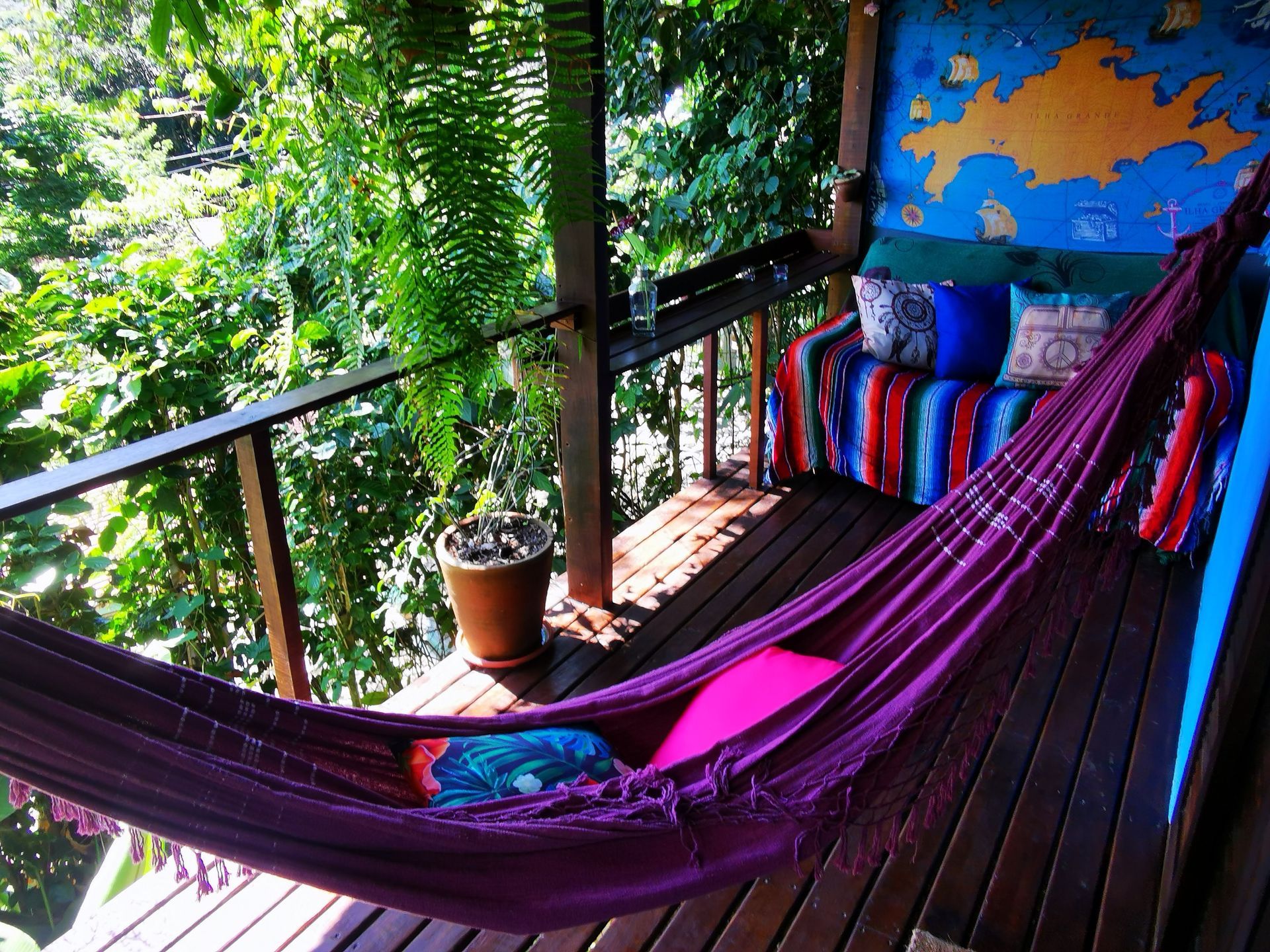 Cozy balcony in Ilha Grande with a purple hammock, colorful cushioned sofa, and potted plants, surro