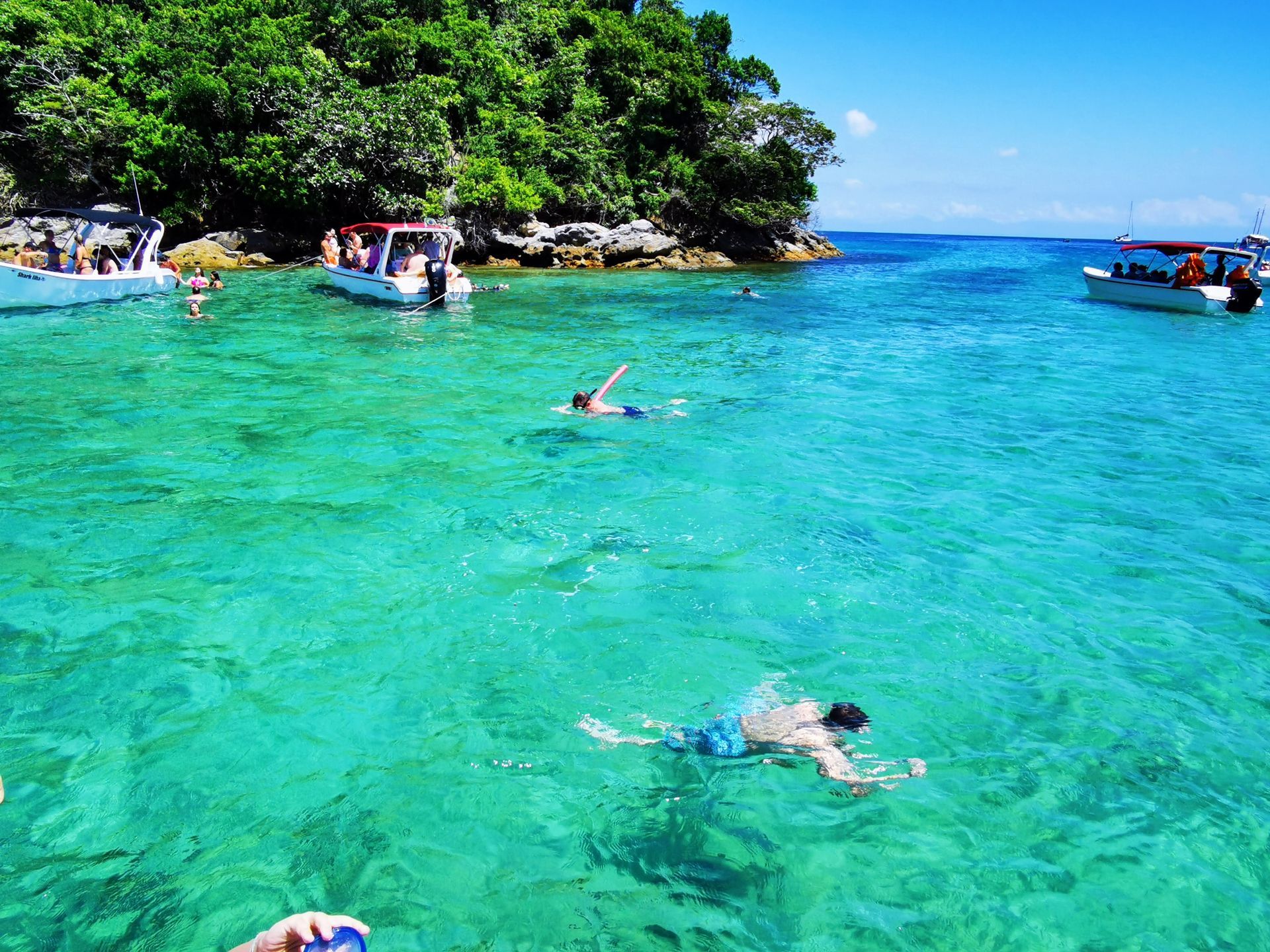 Snorkeling in the crystal-clear waters of Ilha Grande, Brazil, with swimmers exploring vibrant marine life near anchored boats and lush green islands, creating the perfect tropical adventure setting.