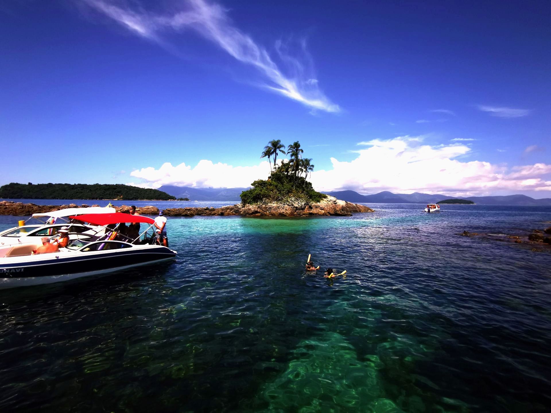 Crystal-clear waters at Ilhas Botinas, near Ilha Grande, with boats anchored and people snorkeling, surrounded by small islands with palm trees and a stunning tropical seascape under a vibrant blue sky