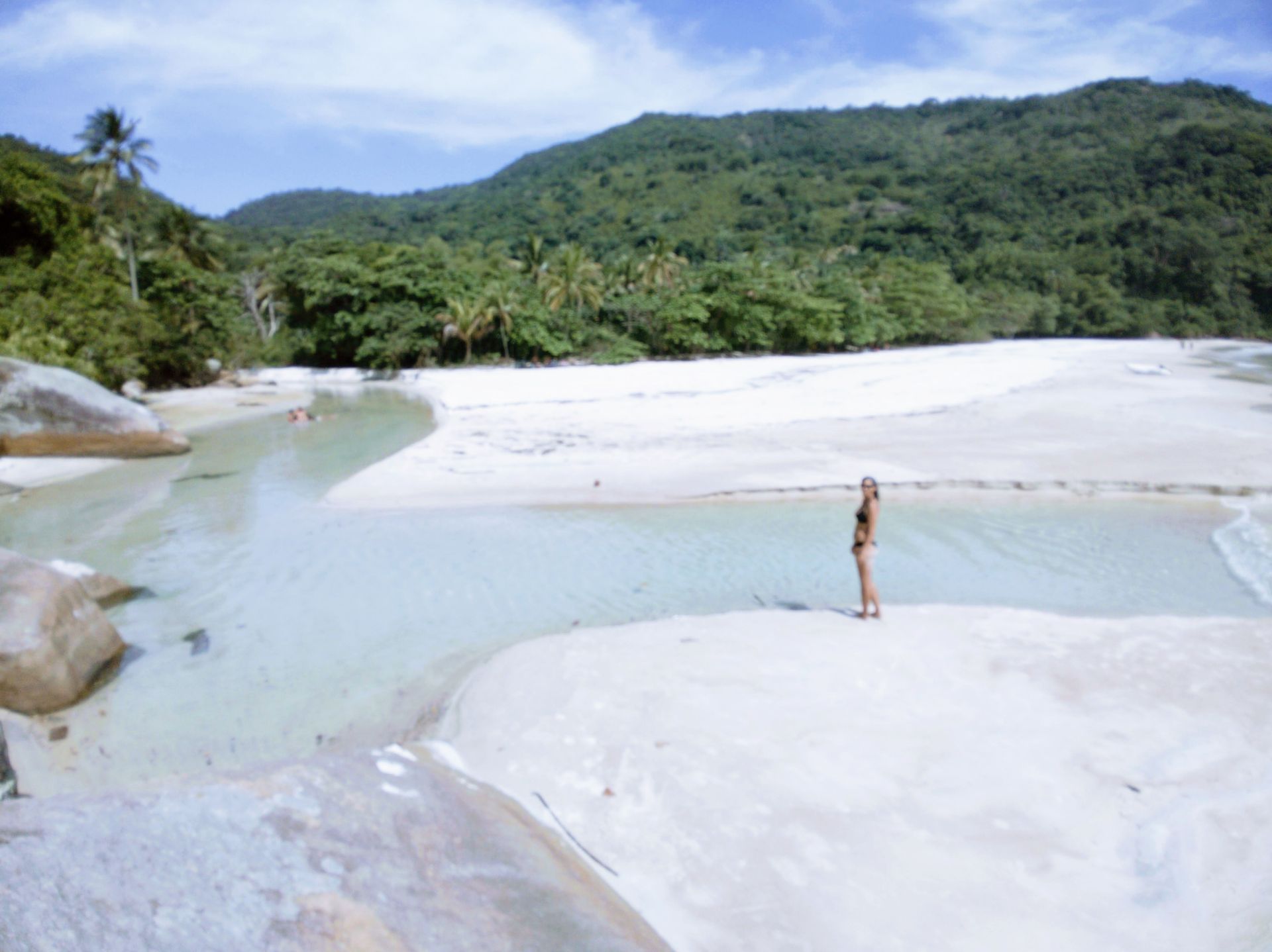 Scenic view of a visitor enjoying the natural beauty at Lopes Mendes, Ilha Grande, with clear shallow waters, lush green hills, and a pristine sandy beach in the background