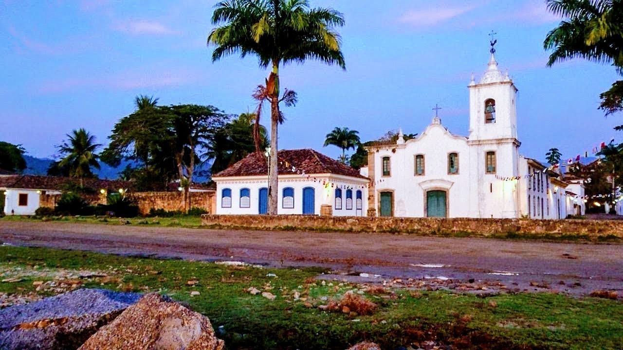 Colonial church and historic buildings in Paraty, Rio de Janeiro, with palm trees and colorful festive flags at dusk.