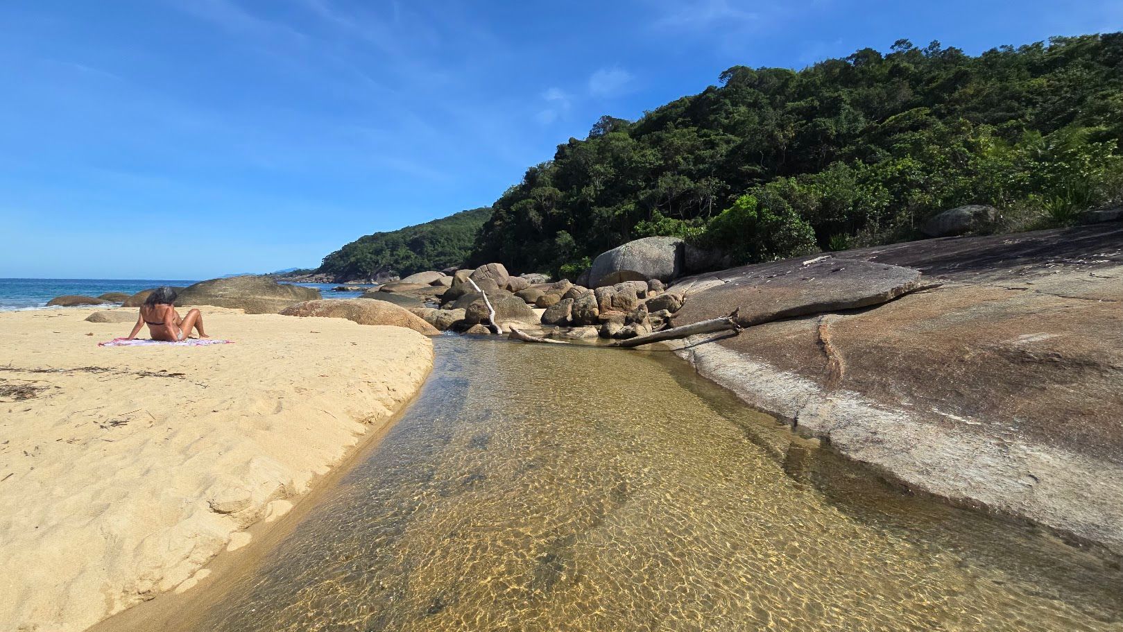 Parnaioca Beach in Ilha Grande, with golden sand, rocks by the shore, calm sea and Atlantic Forest in the background