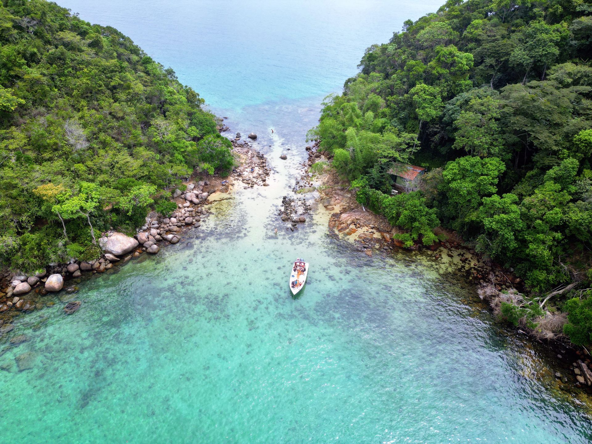 Vista aérea da Lagoa Verde, Ilha Grande, Brasil, com águas cristalinas em tons de turquesa, um barco ancorado próximo à costa e uma exuberante floresta tropical ao redor da enseada rochosa, tornando o local perfeito para snorkeling e natação