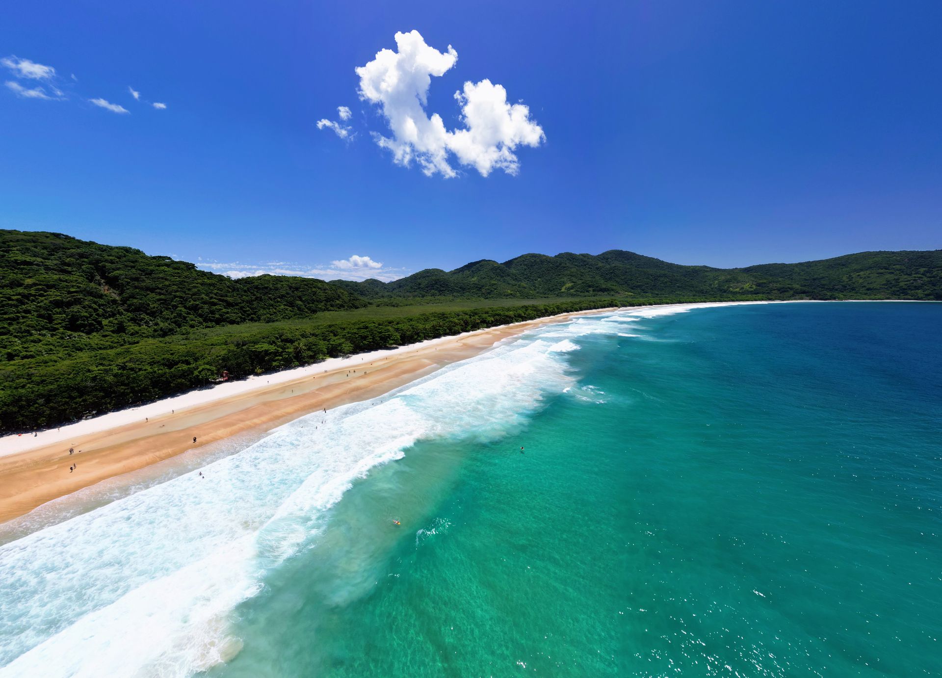 Aerial view  of a pristine tropical beach with golden sand, turquoise waves, and lush green forest in the background, showcasing the untouched beauty of Ilha Grande, Brazil