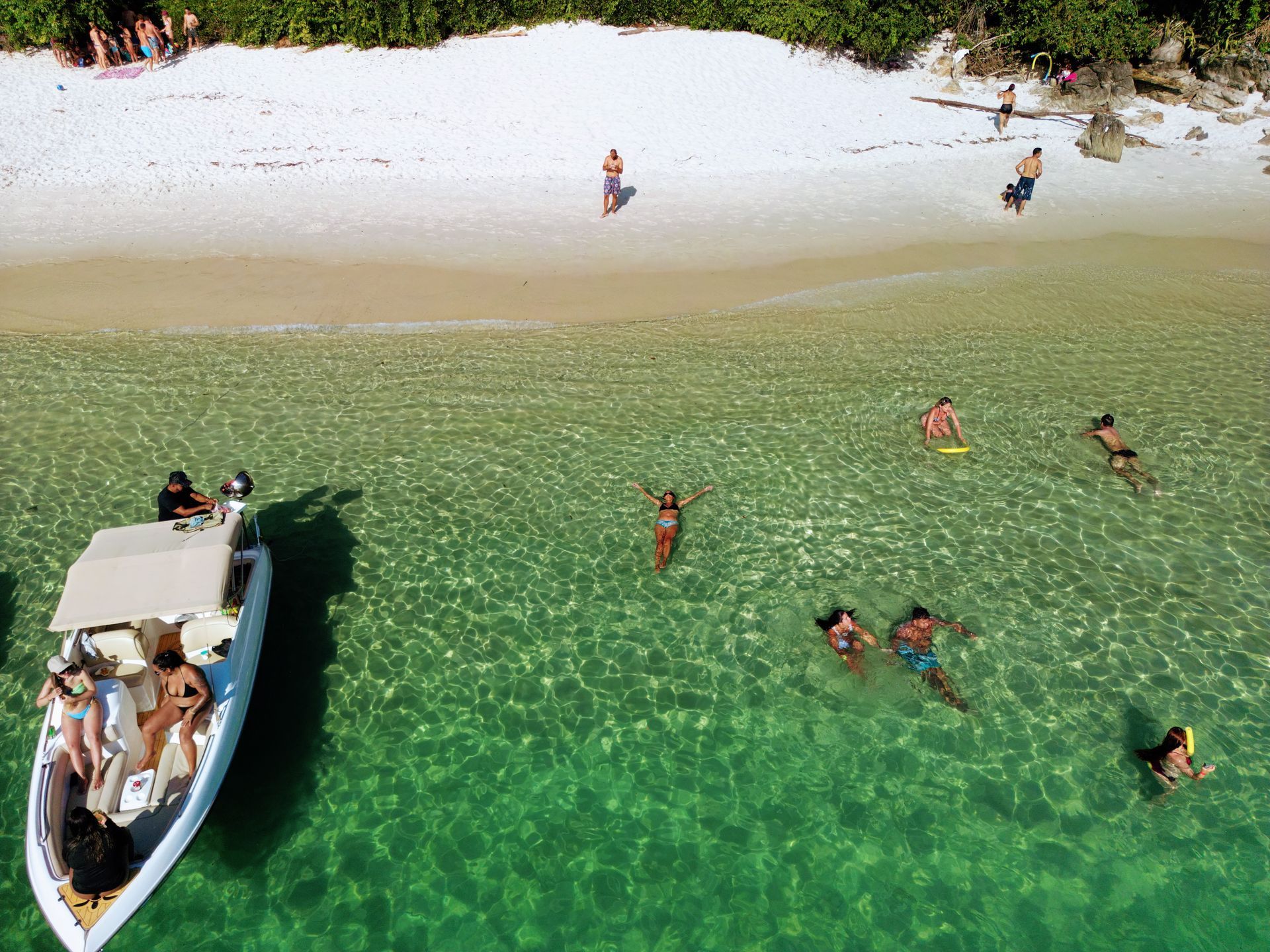 Vista aérea de uma praia tropical com águas cristalinas, onde pessoas nadam e relaxam perto de um barco ancorado próximo à costa, destacando o cenário paradisíaco da Ilha Grande, Brasil.