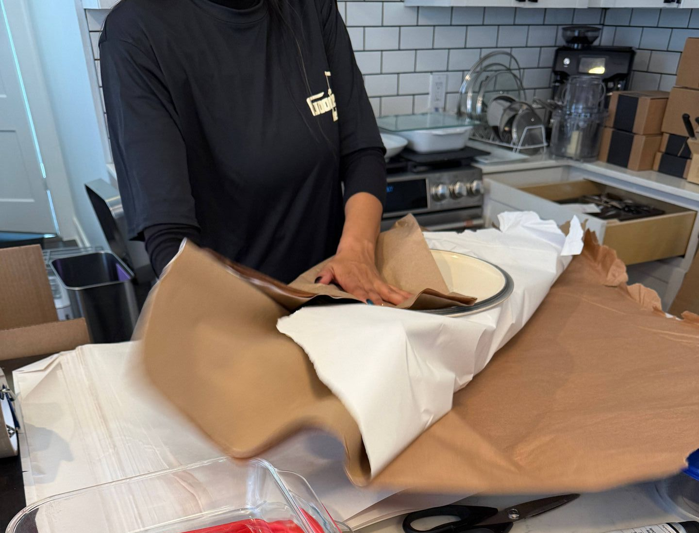 A person is wrapping a casserole dish with a box of hetty strong baking paper.