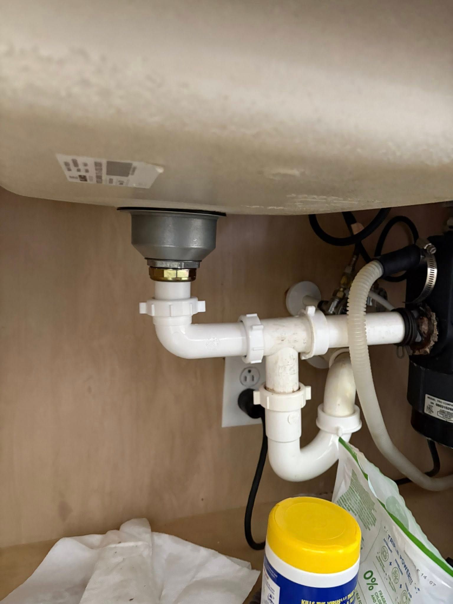 White kitchen sink drain pipes under a beige cabinet. Garbage disposal on the right.