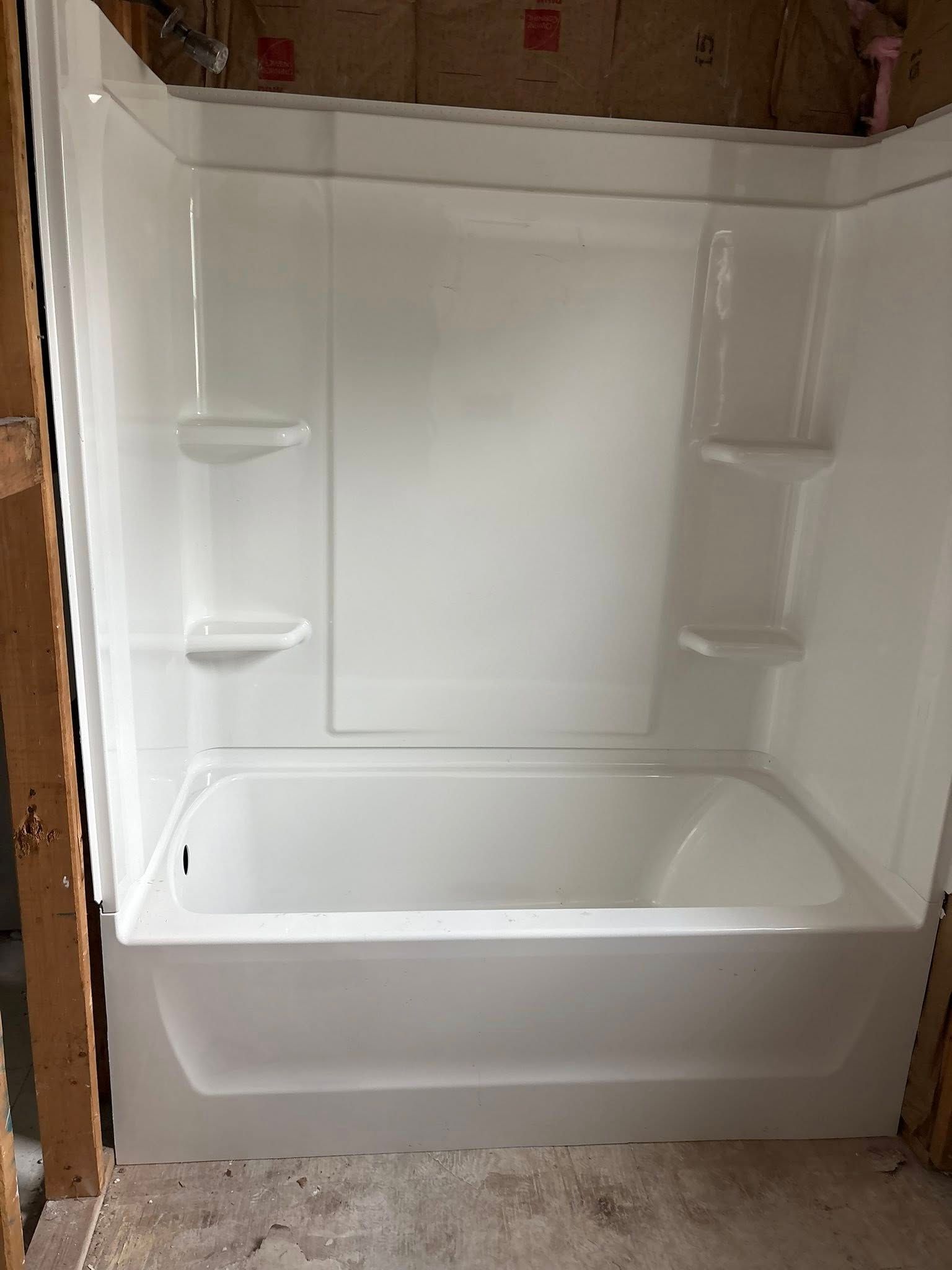 White bathtub and shower surround installed in a room under construction.