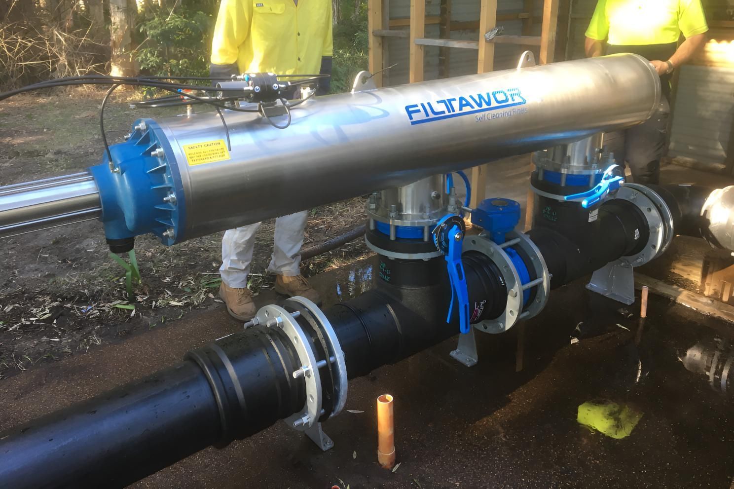 A Man is Standing Next to a Pipe With a Filter Attached to It — Sweeney's Pumps & Irrigation In Medowie, NSW