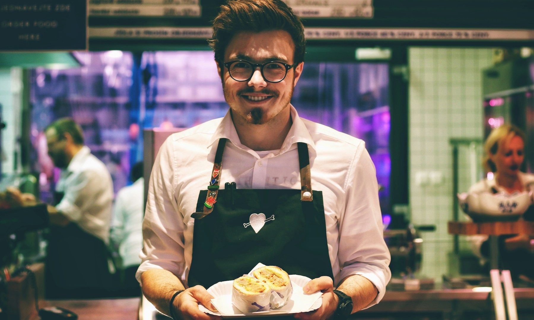 A man in an apron is holding a tray of food in a restaurant.