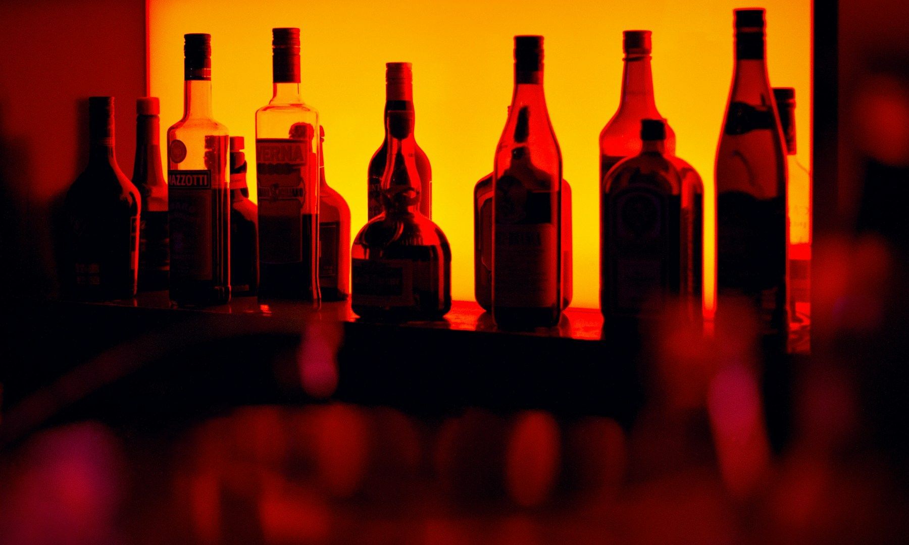 A row of bottles of alcohol are lined up on a bar shelf.