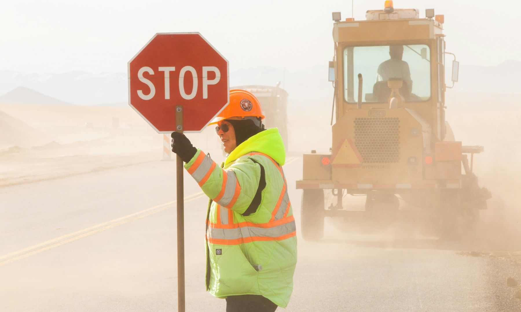A man is holding a stop sign in front of a bulldozer.