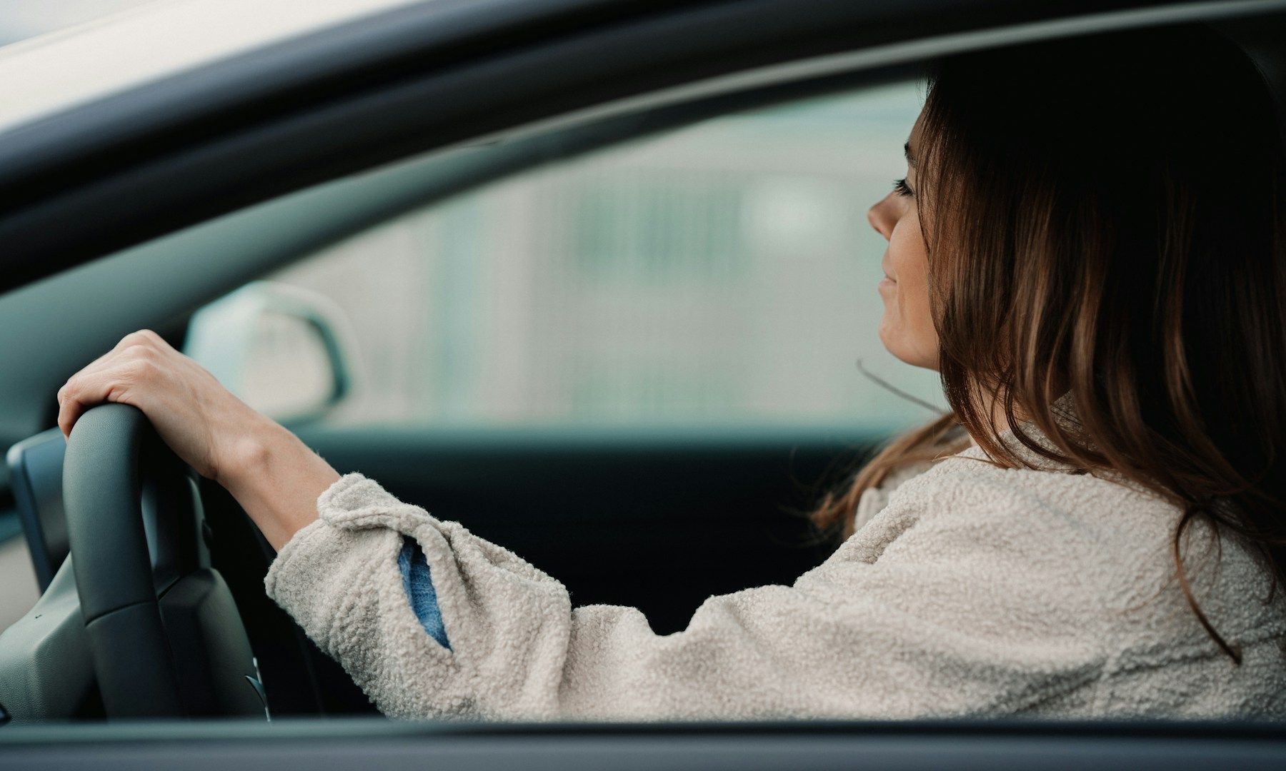 A woman is driving a car and looking out the window.