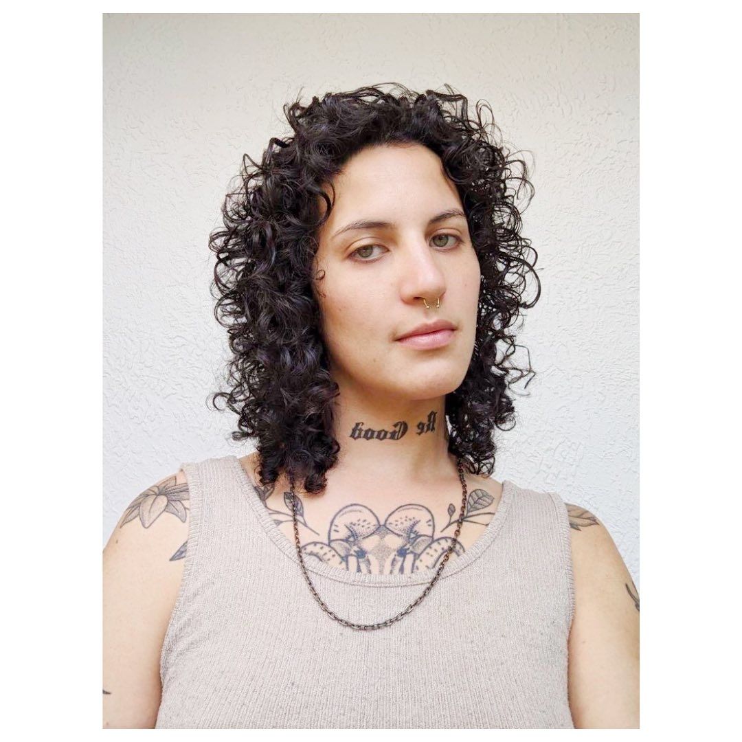 A woman with curly hair has a tattoo on her neck that says good life