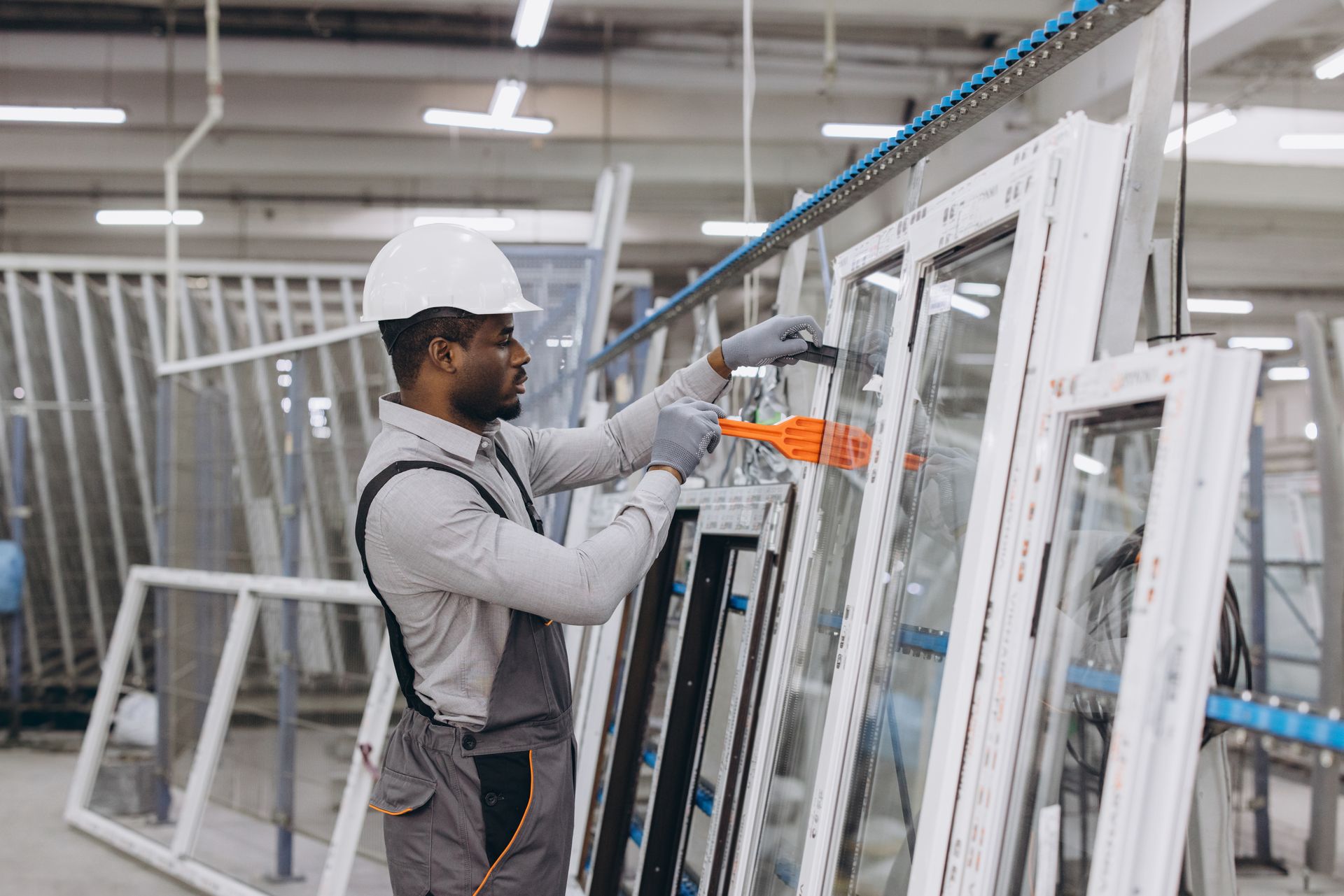 Factory worker in white hard hat dusting window frames. Factory worker in white hard hat dusting window frames.