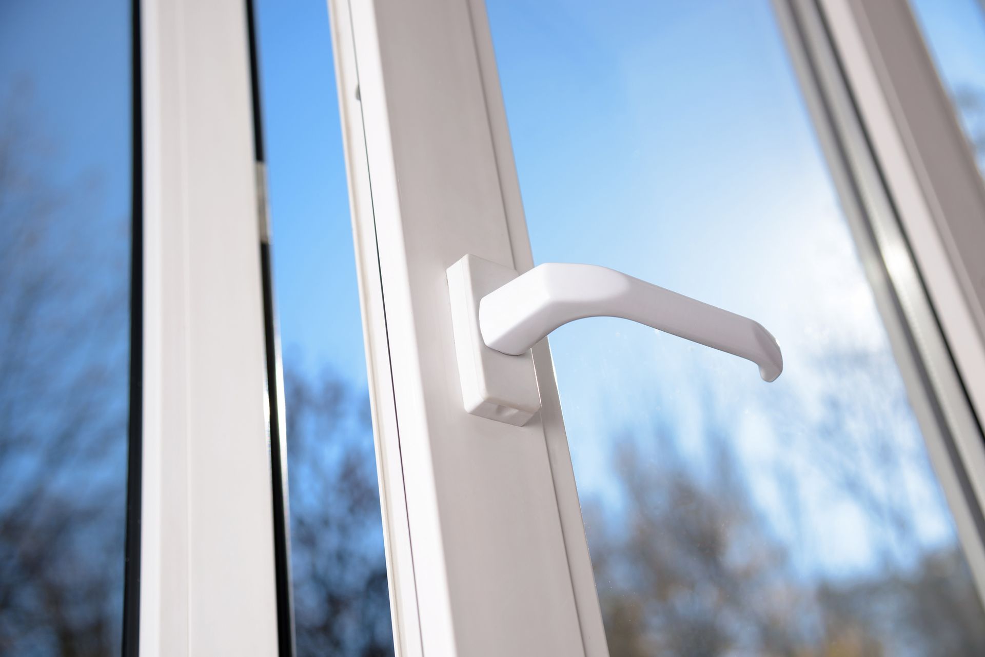White window handle on white window frame with a blue sky background.