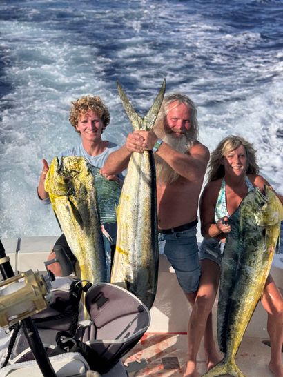 A man and two women are holding large fish on a boat.