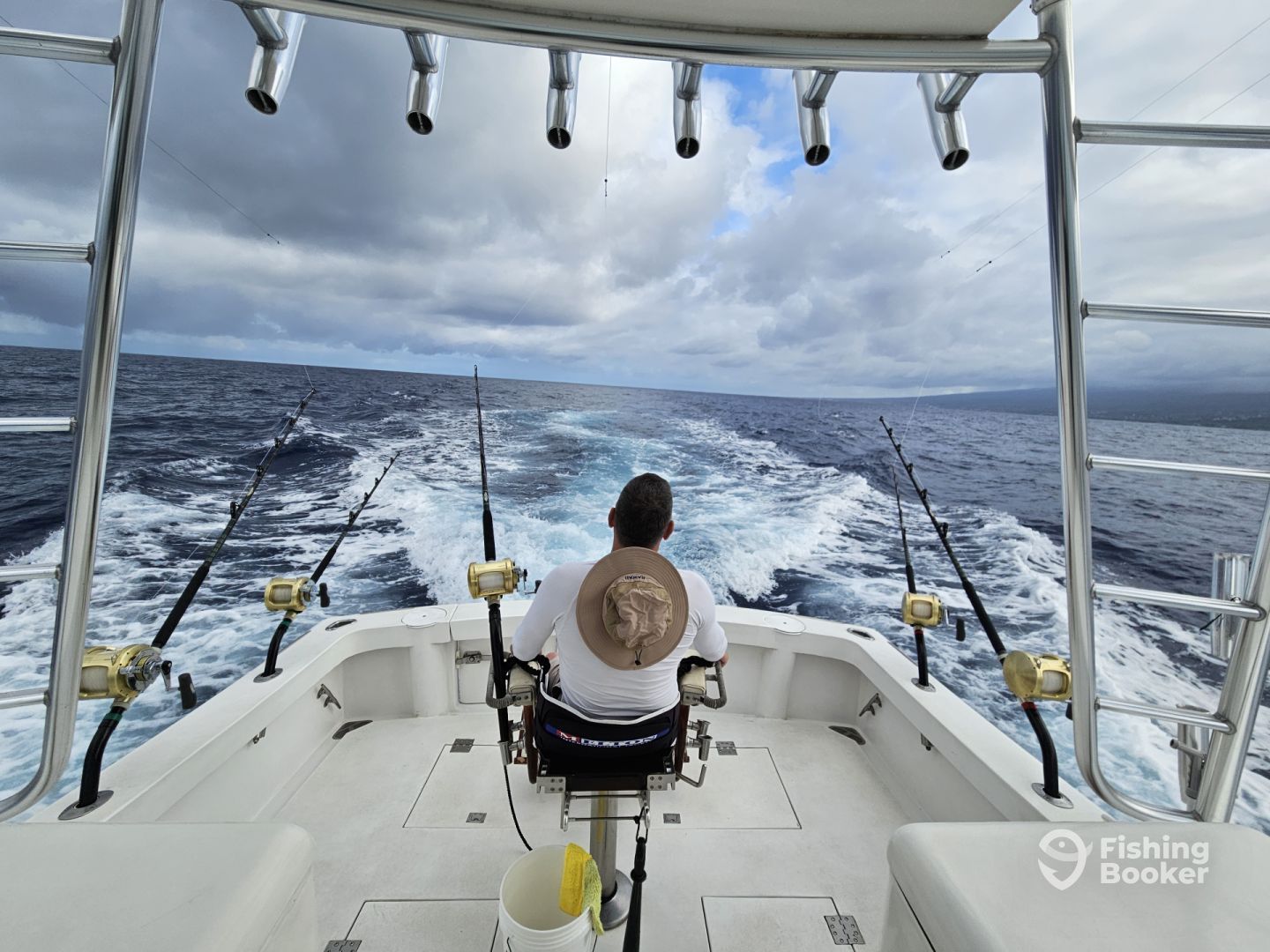 A man is sitting on the back of a boat fishing in the ocean.