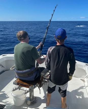 Two men are fishing on a boat in the ocean.