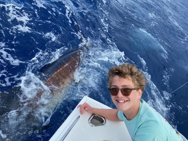 A young boy is on a boat in the ocean with a large fish in the background.