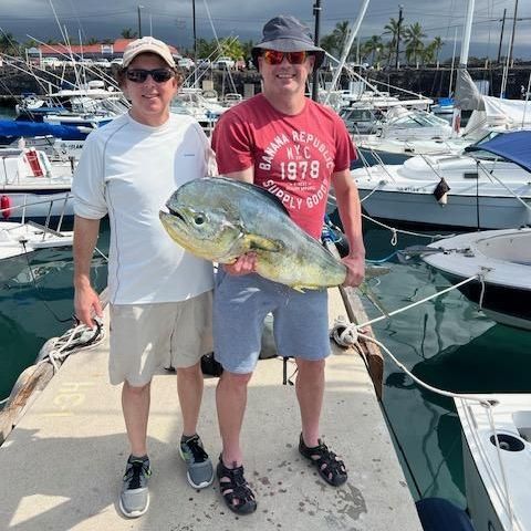 Two men are standing on a dock holding a fish and one has a shirt that says 1978