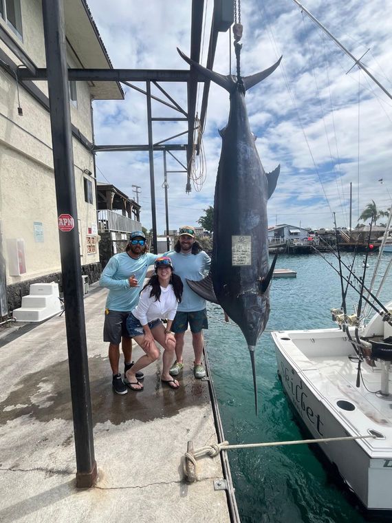 A group of people standing next to a large fish on a dock.