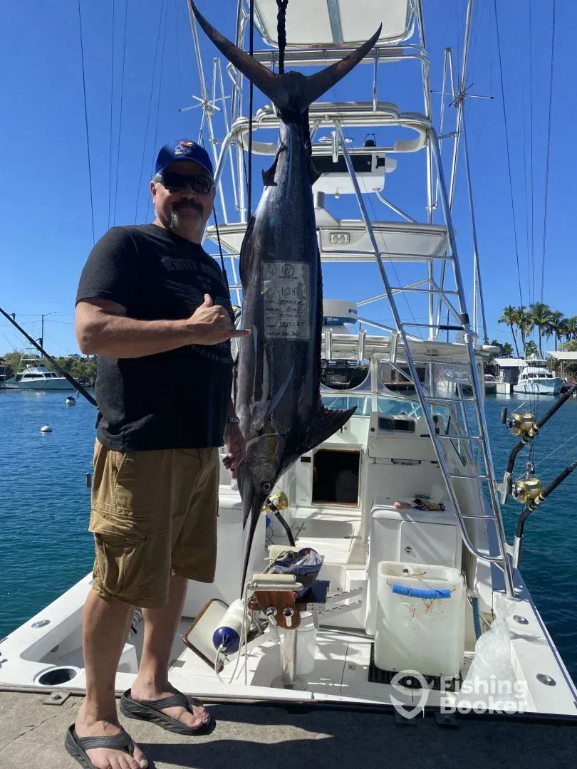 A man is standing on a boat holding a marlin fish.