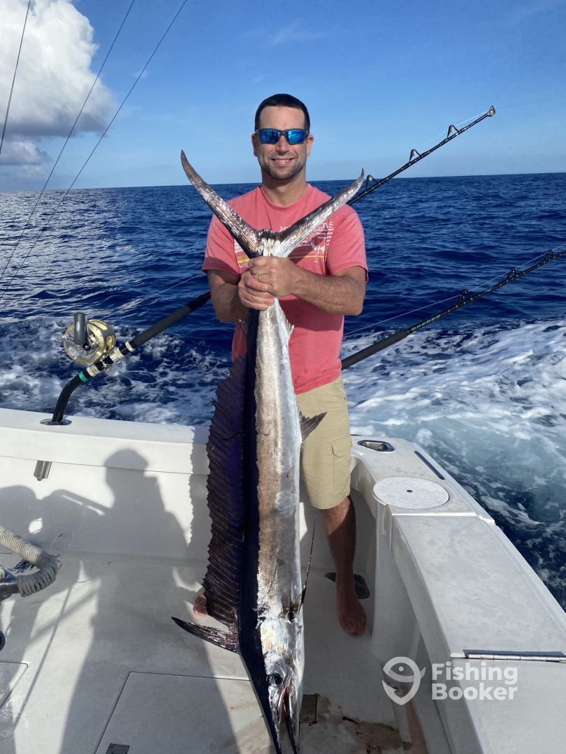 A man is holding a large fish on a boat in the ocean.