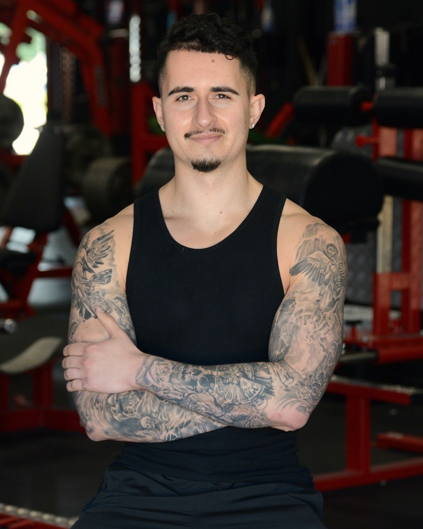 Experienced personal trainer standing confidently with arms crossed in a professional gym setting, dedicated to helping clients build strength and reach their fitness goals