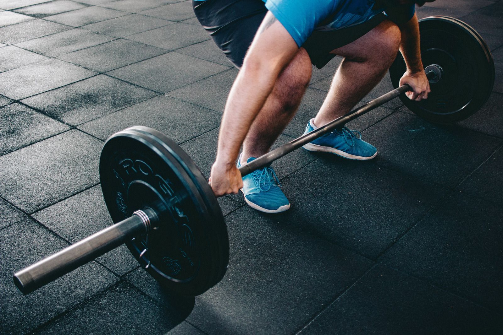A person is squatting down to lift a barbell in a gym.