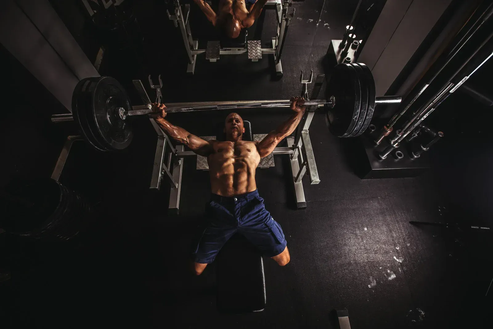 A man is lifting a barbell on a bench in a gym.