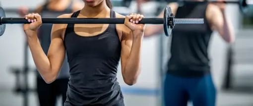 A woman is lifting a barbell over her head in a gym.