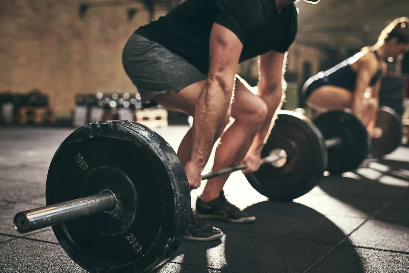 A man is squatting down to lift a barbell in a gym.