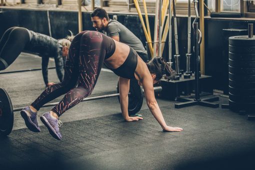A man and a woman are doing push ups in a gym.