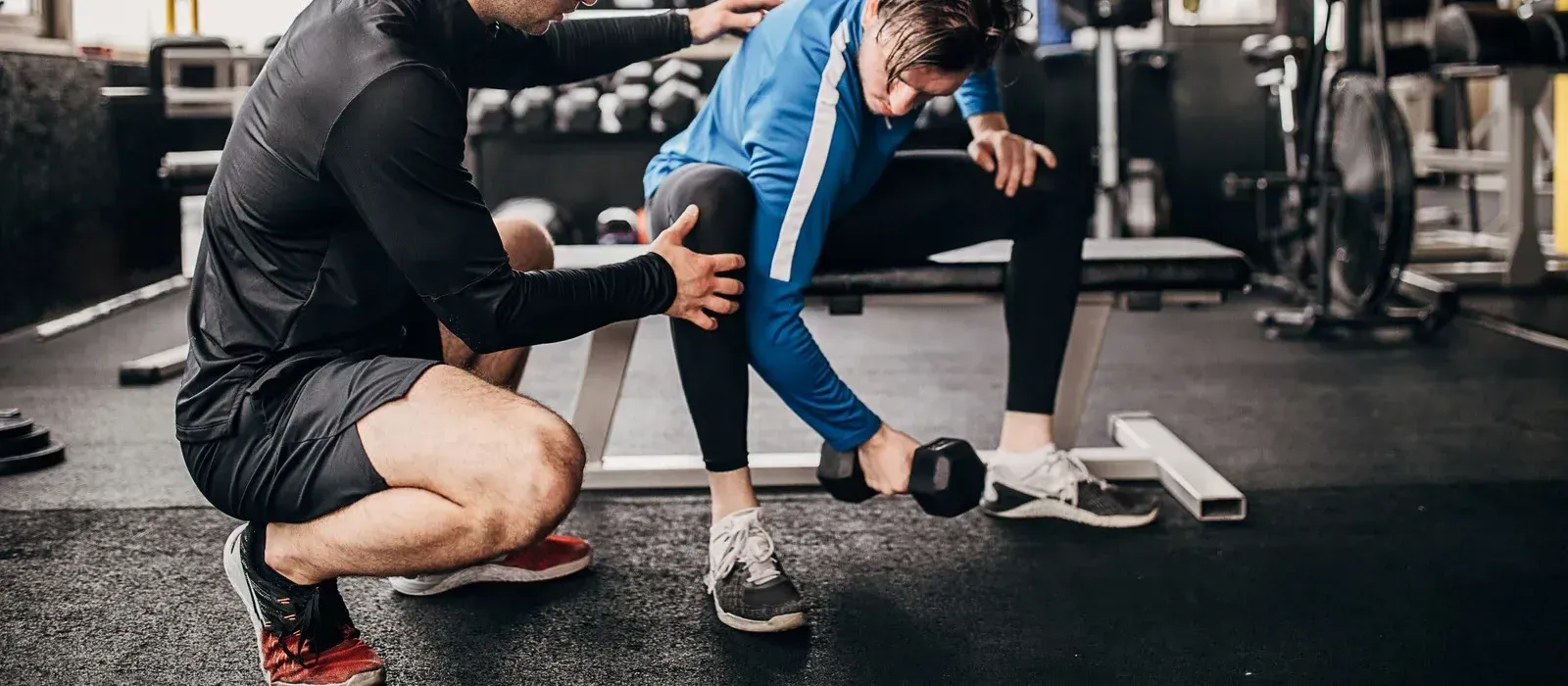 A man is helping a woman lift a dumbbell in a gym.