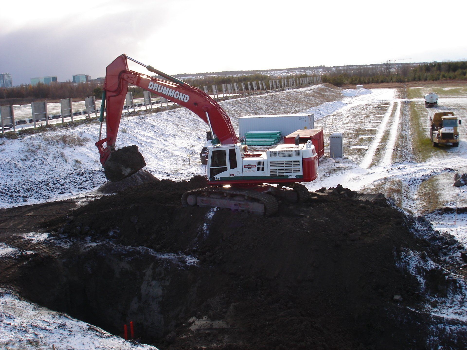 Red excavator digging earth in snowy, outdoor setting.