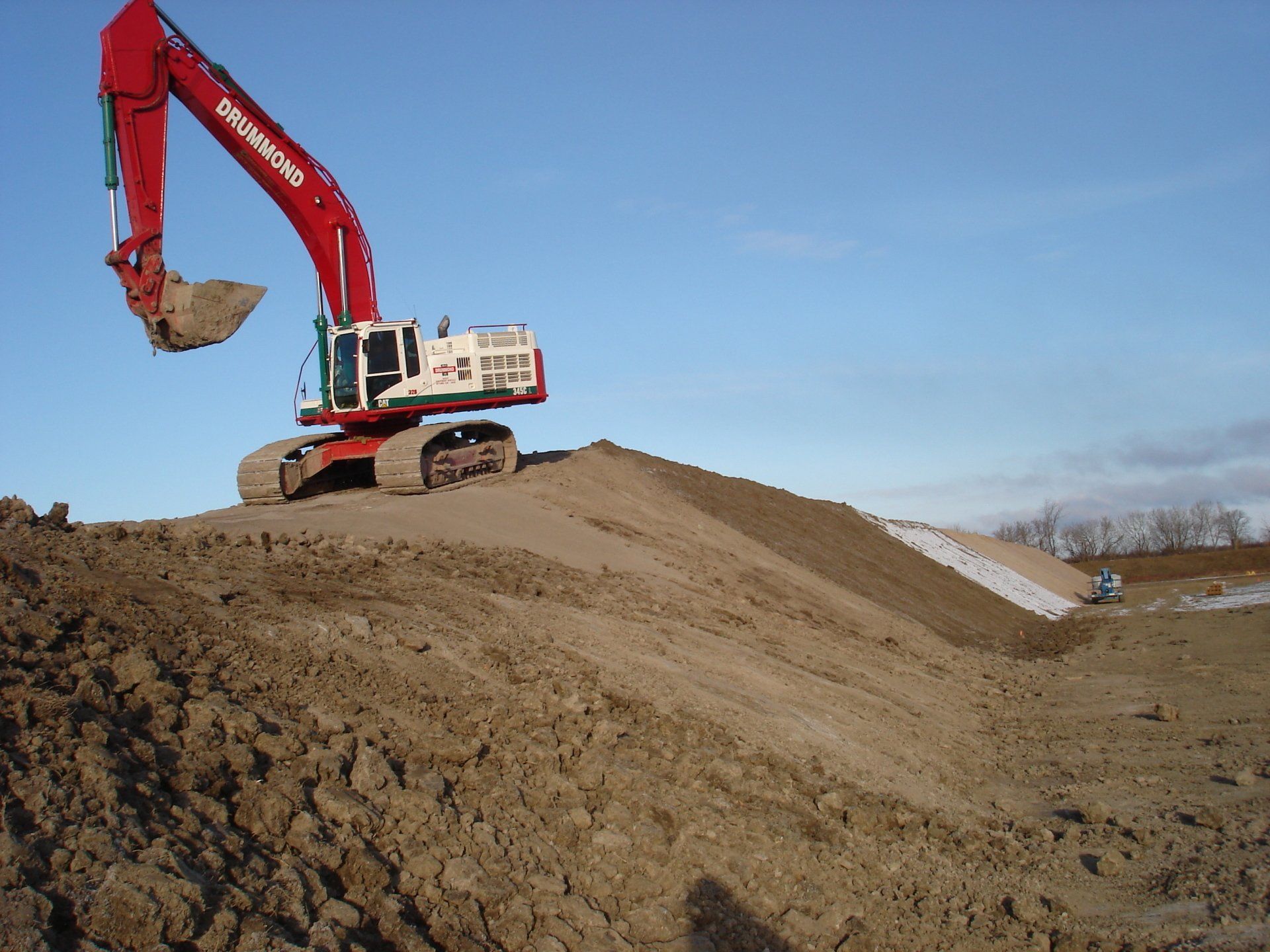 Red excavator on a pile of dirt, working outdoors under a blue sky.