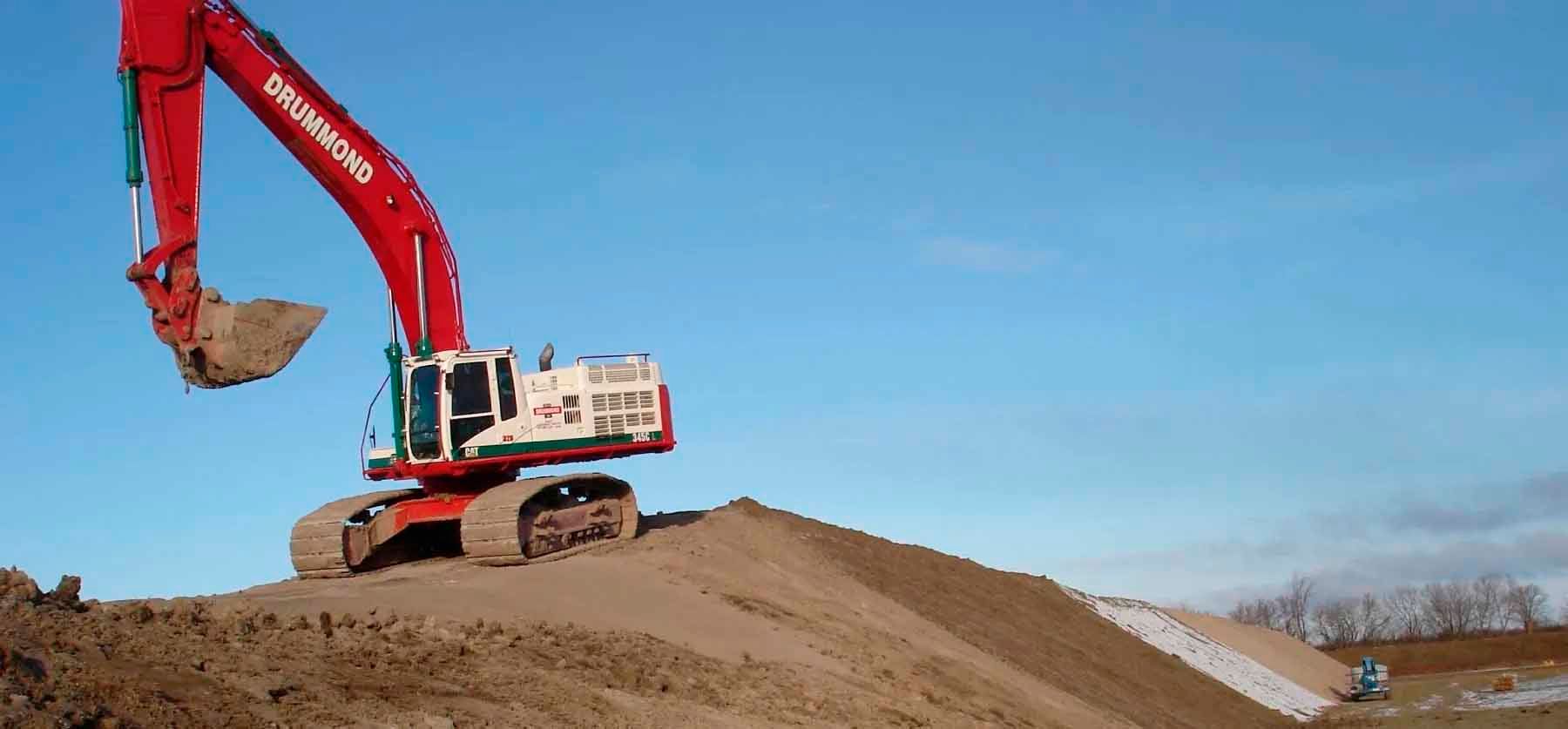 A red excavator on a dirt pile against a clear blue sky.