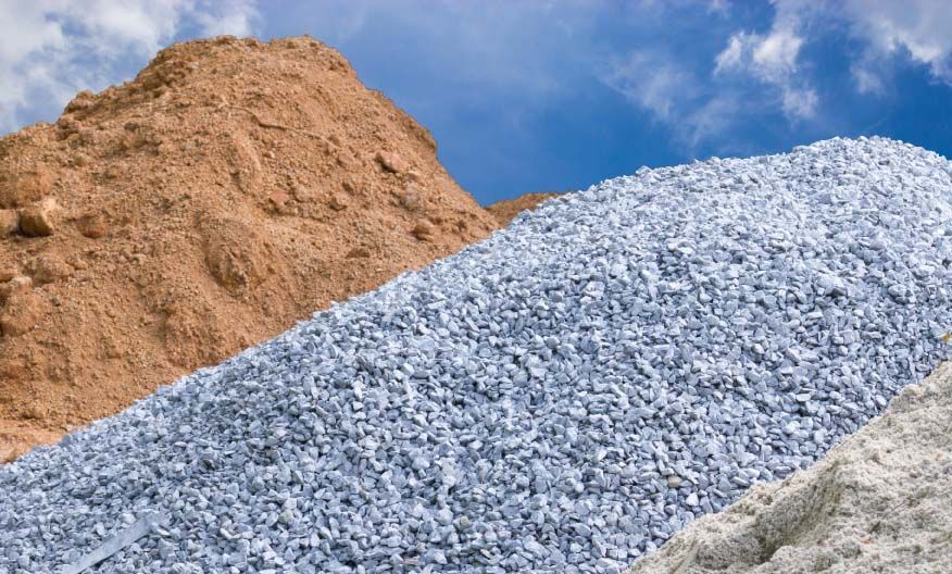 Piles of brown sand, blue gravel, and white sand against a blue sky.