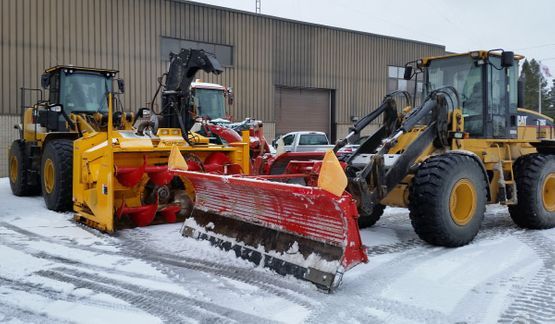 Yellow snowplow machinery parked, ready to clear snow in front of a building.