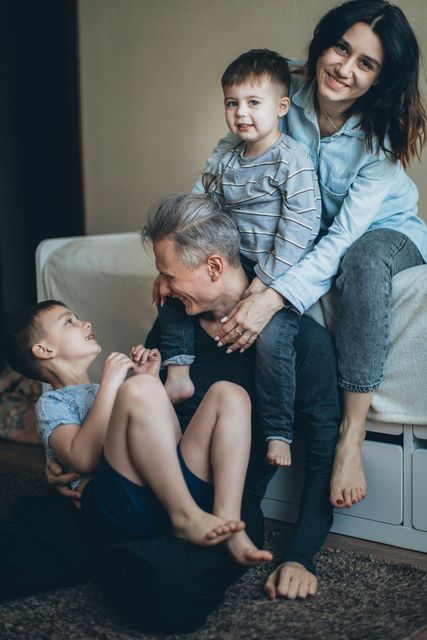 Four family members in a cozy living room, smiling and playing together on a couch and floor.