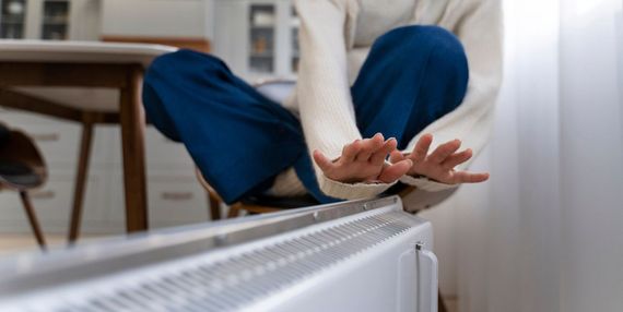 Une personne se réchauffant les mains sur un radiateur dans une pièce.