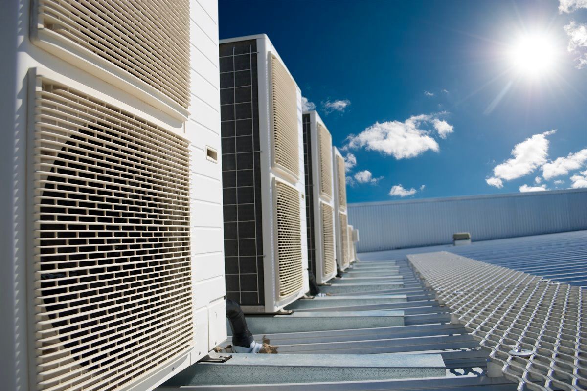 Unités de climatisation sur un toit, ciel bleu ensoleillé en arrière-plan.