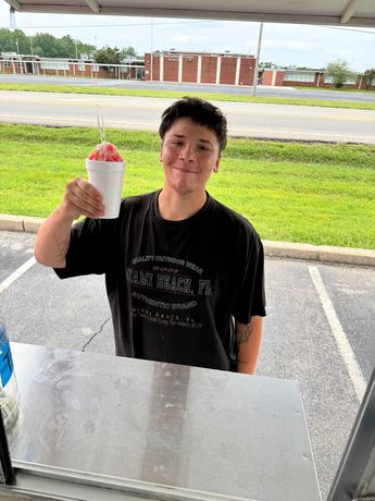 Person holding a snow cone in front of a snow cone stand