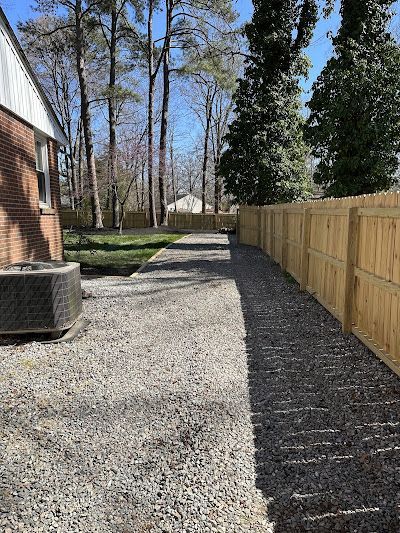 A wooden fence surrounds a gravel driveway leading to a house.