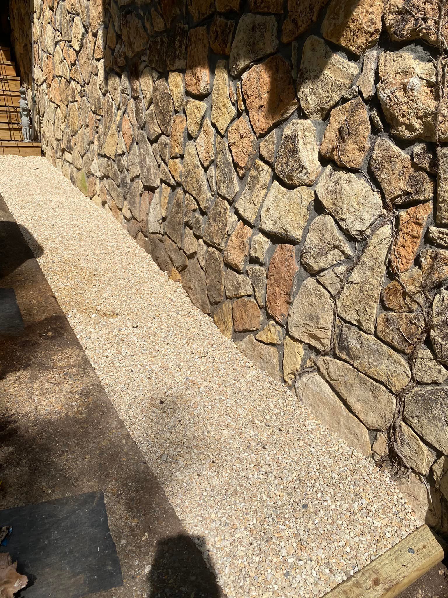 A stone wall with a gravel walkway in front of it.
