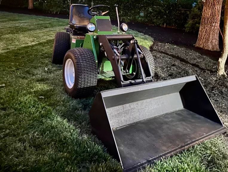 A green lawn mower with a black bucket attached to it
