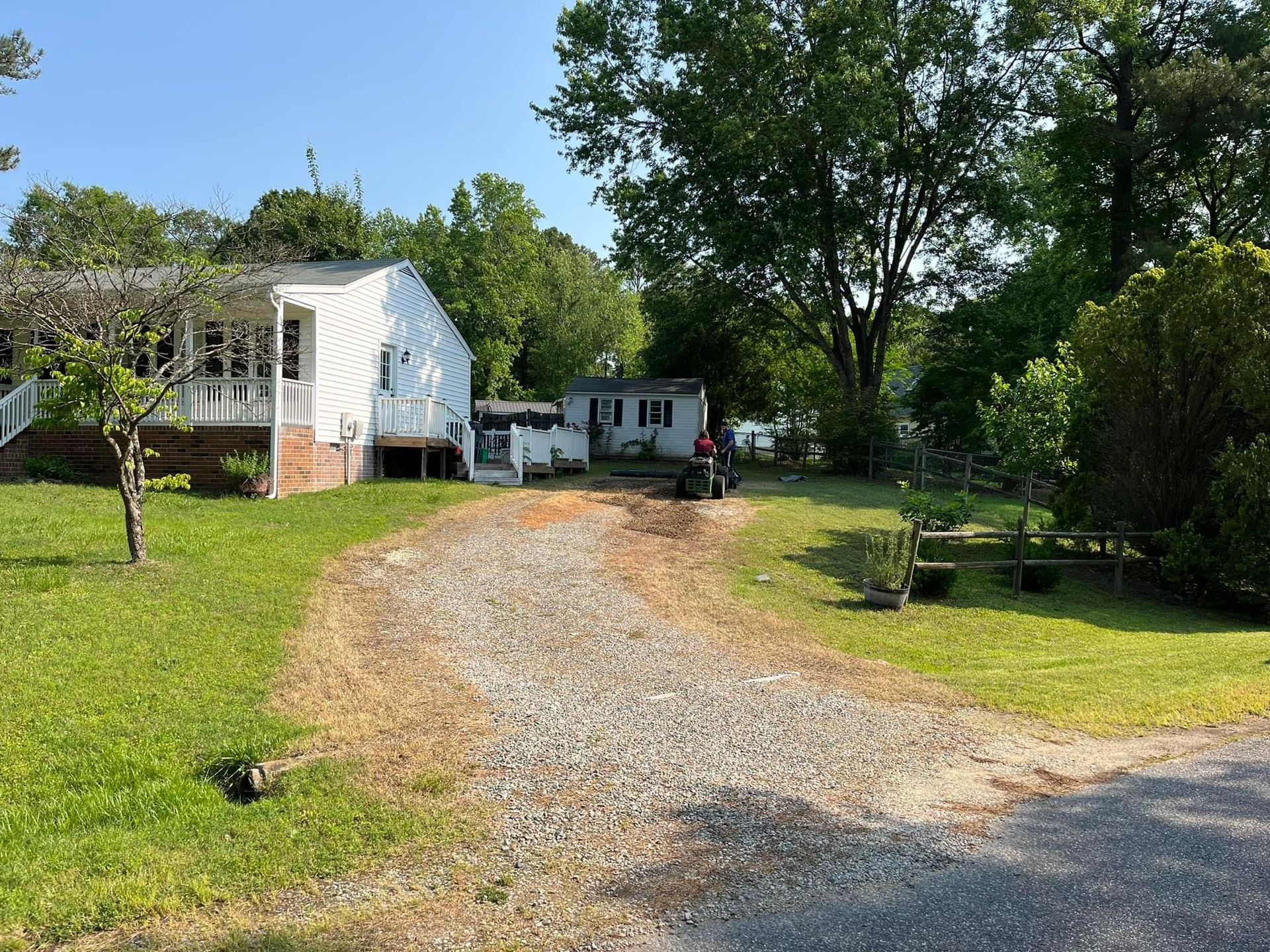 A dirt road leading to a white house surrounded by grass and trees.
