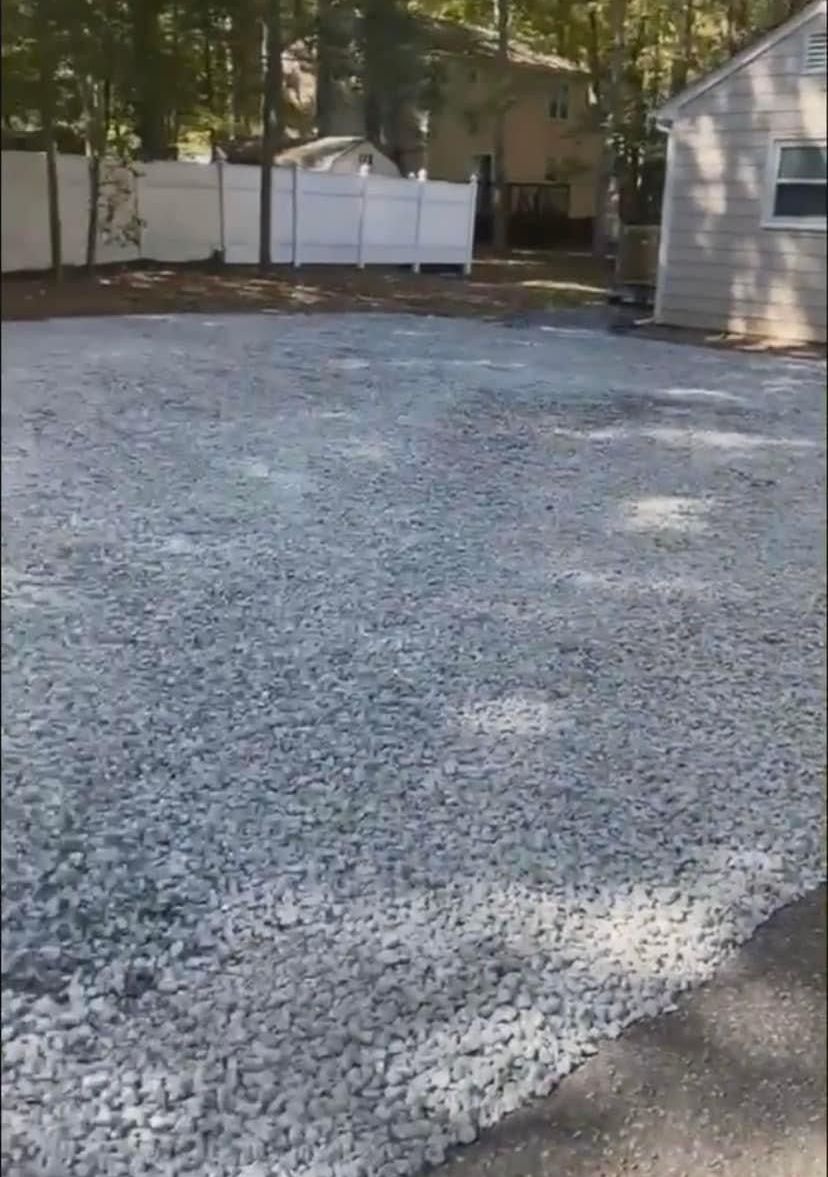 A gravel driveway with a white fence and a house in the background.