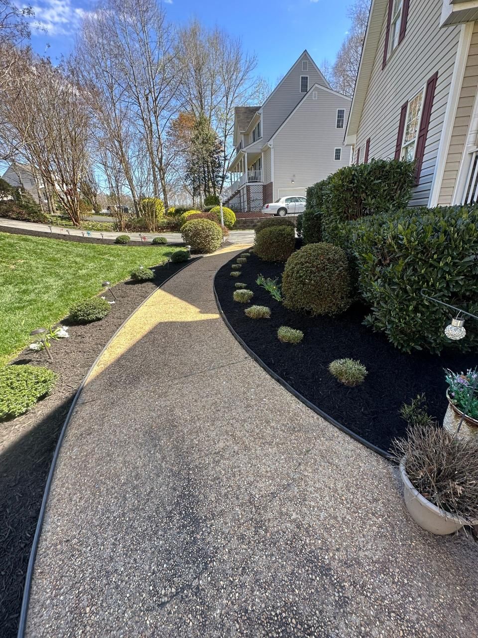 A walkway leading to a house with a lot of bushes and trees.